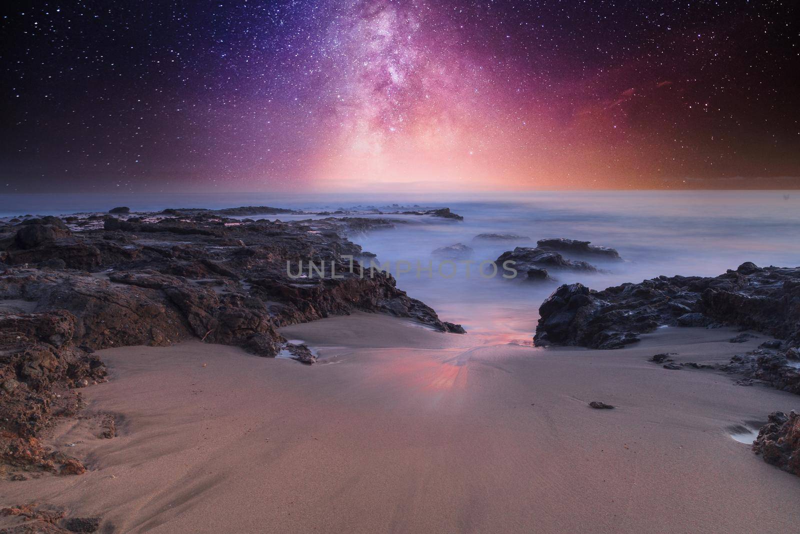 Milky way shimmers over the ocean water as it cascades over rocks in Reykjavik, Iceland.