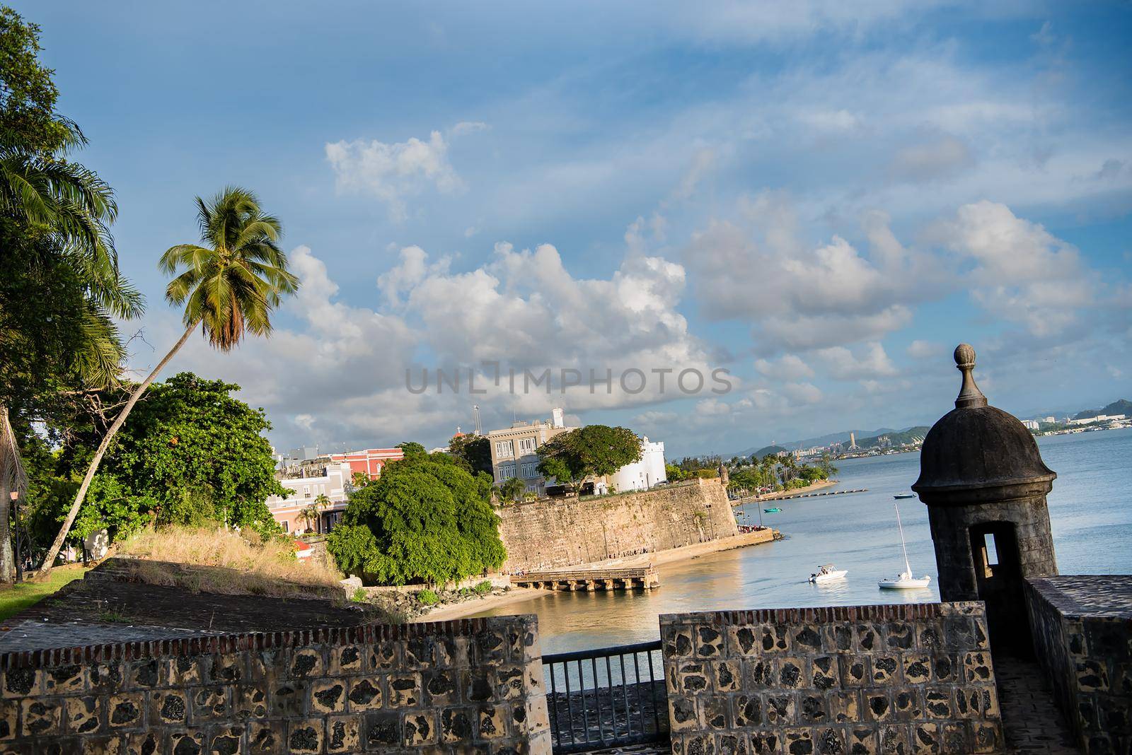 Gorgeous view of San Juan, Puerto Rico city scape with historic brick, palm trees, water, and blue skies.