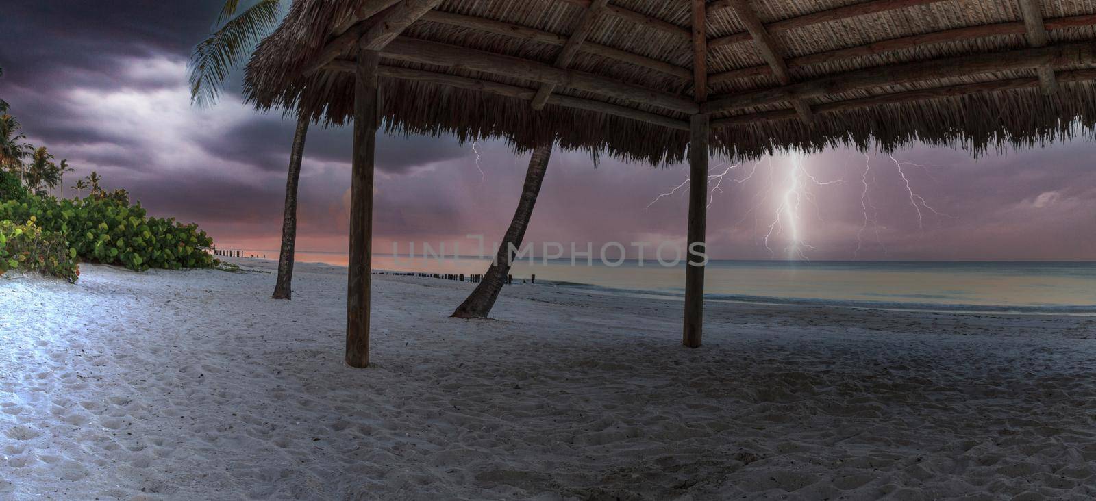 Lightning storm over a tiki at the ocean at Port Royal Beach in Naples, Florida at sunrise.