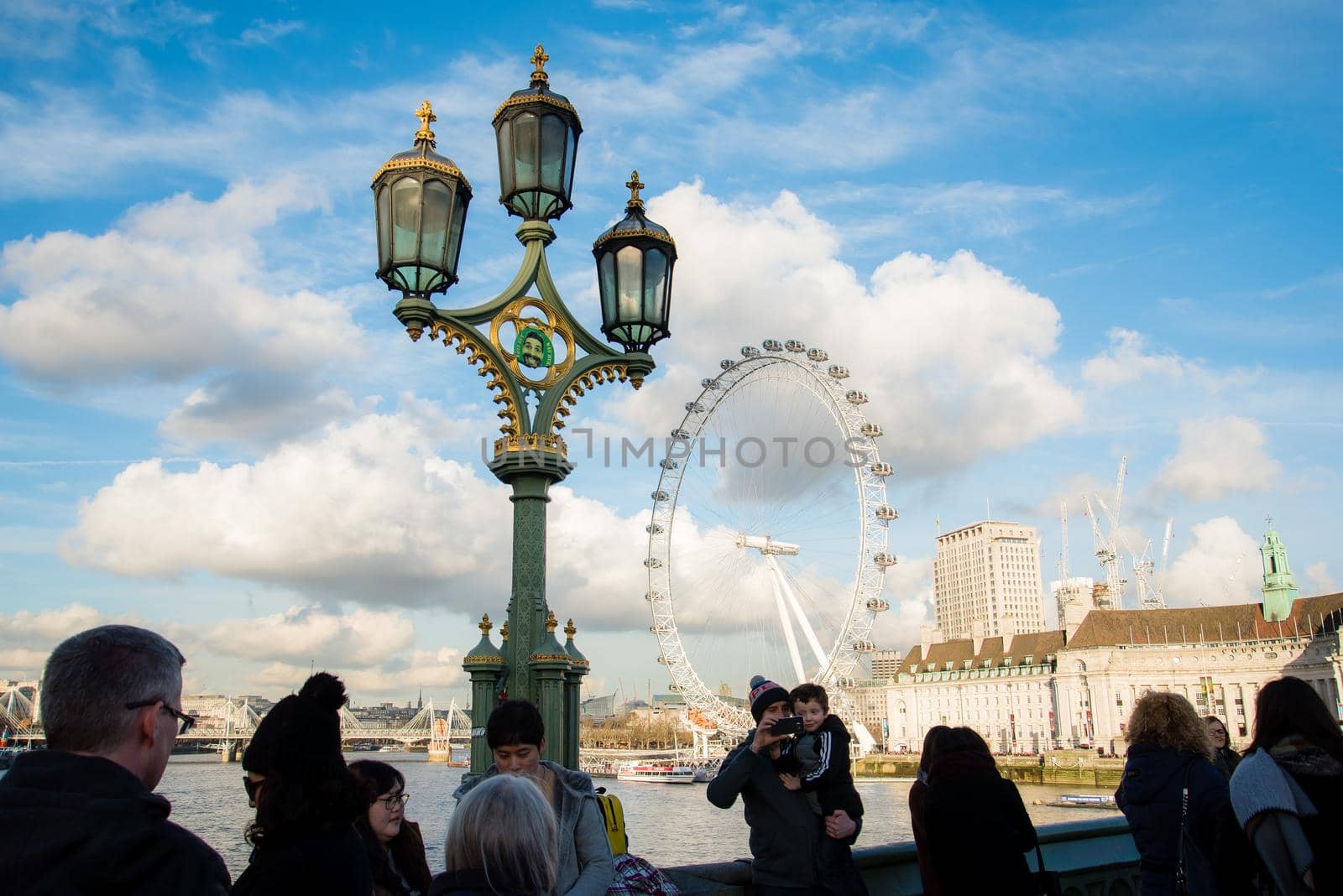 London, UK - February 4, 2017: View of tourists from the back looking out at the London Eye on a gorgeous day with blue skies and big puffy clouds.