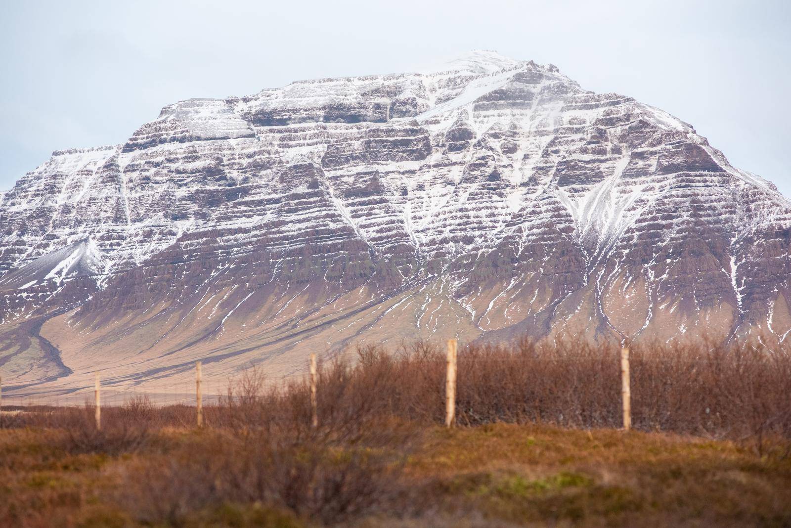Colorful snow capped mountain showing off textures and layers Icelandic landscape with fence line by jyurinko