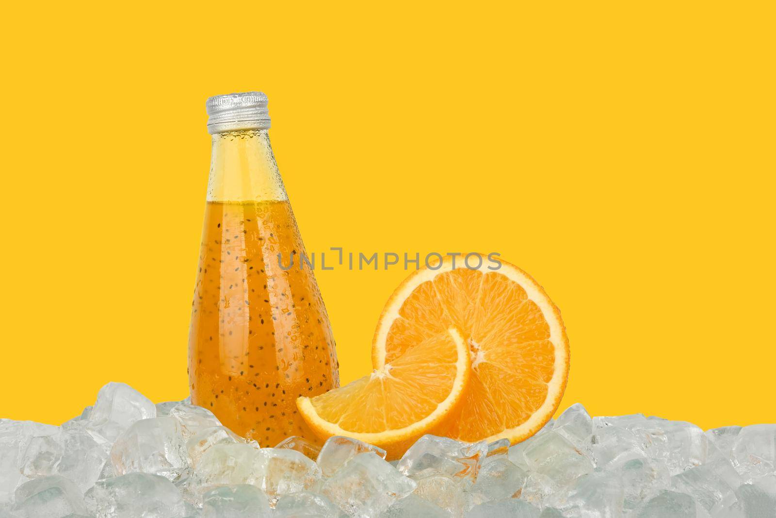 Close up one glass bottle of cold orange juice cocktail drink with chia seeds and half cut orange on ice cubes isolated on yellow background, low angle side view