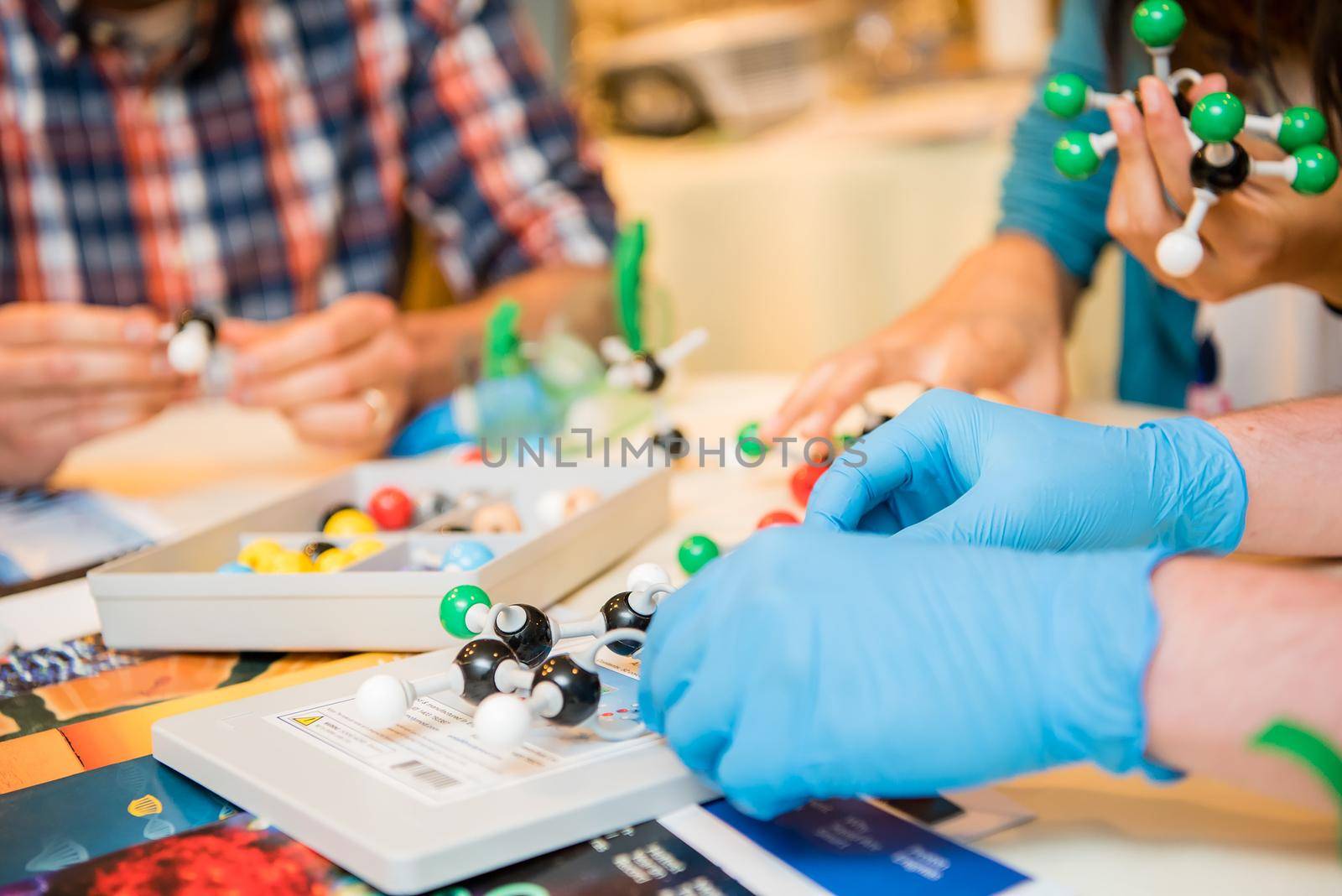 Up close view of young scientists wearing blue latex gloves working on an experiment with colorful DNA balls.