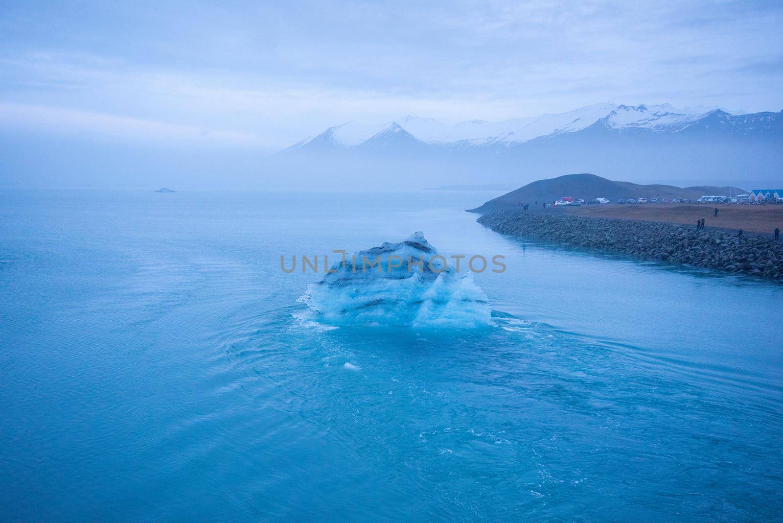 Icelandic glacier floating from global warming effects. Foggy atmosphere with snowcapped mountain range in the distance. Iceberg has layers of volcanic ash.