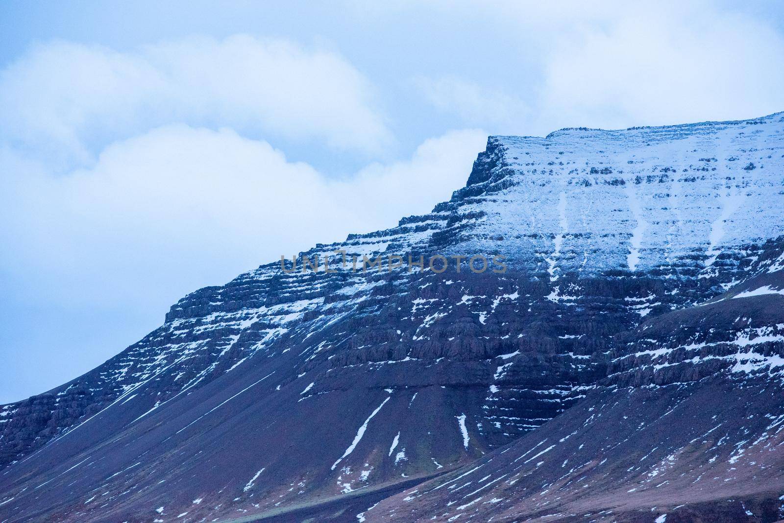 Close up of snow capped black mountain ridges in Iceland with clouds to add depth.