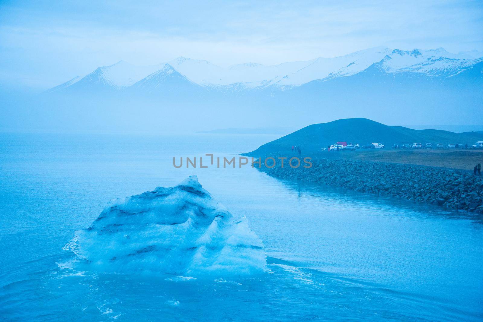 Icelandic glacier floating from global warming effects. Foggy atmosphere with snowcapped mountain range in the distance. Iceberg has layers of volcanic ash.