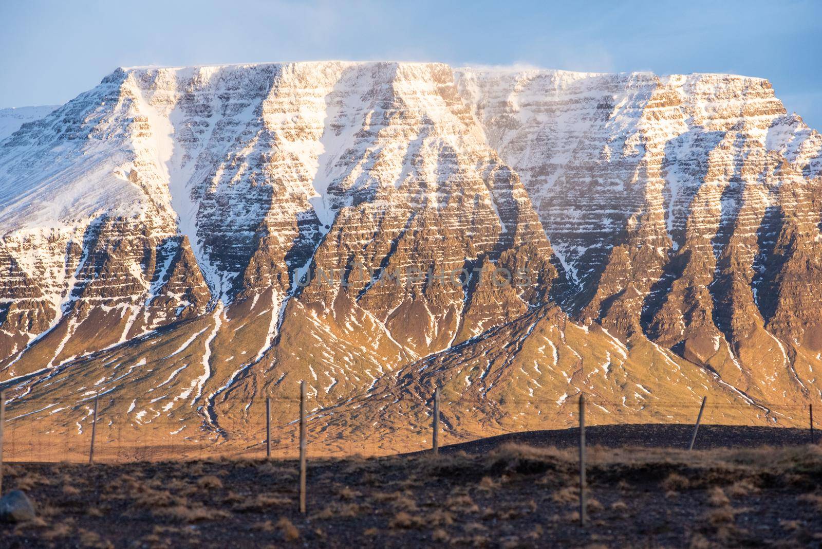 Golden hour lighting close up of geological phenomenon in Iceland snow capped mountain wind blowing freezing texture layers landscape cliff edges wow