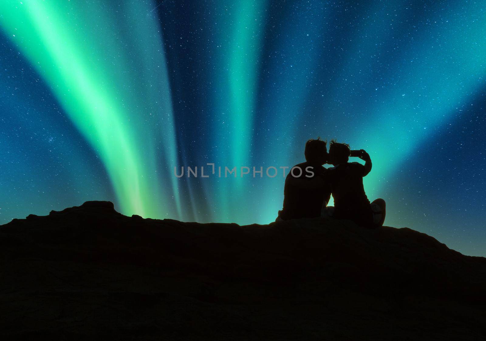 Couple kiss on a rock below the Green Aurora borealis shimmers by steffstarr