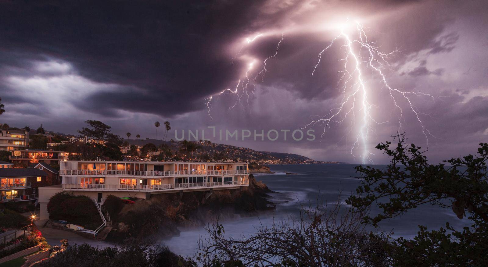 Lightning flashes over a cliff overlooking the ocean in Laguna Beach, California at sunrise.