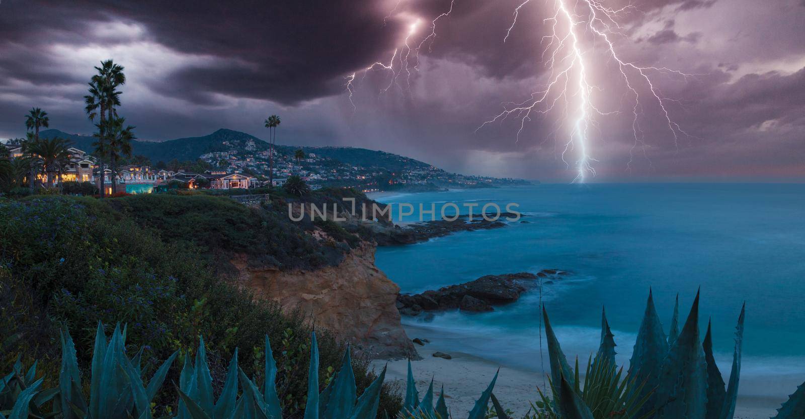 Lightning flashes over a cliff overlooking the ocean in Laguna Beach, California at sunrise.