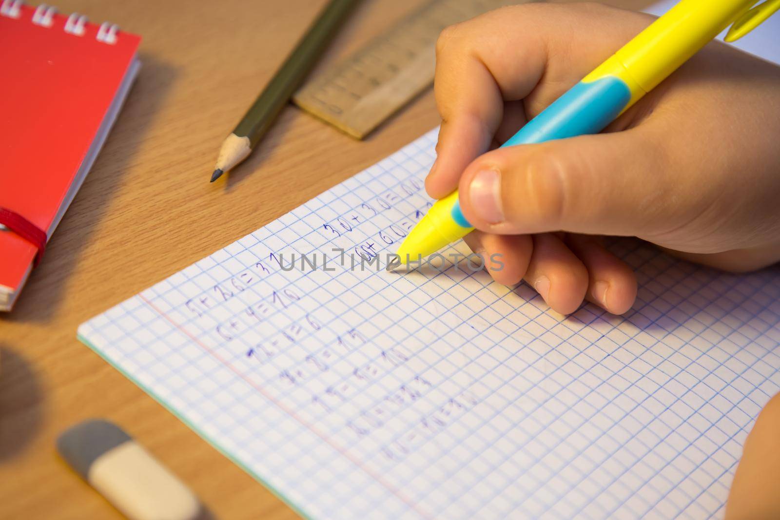 Pupil's hand solves math examples with a ballpoint pen close-up. A schoolboy performs a task at the workplace. The concept of children's education, teaching knowledge, skills and abilities.