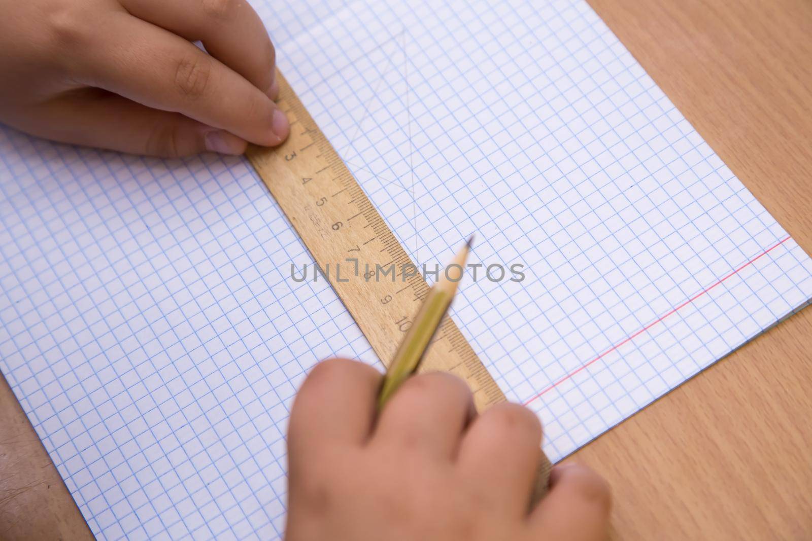 The student pressed a ruler to a notebook sheet, a pencil in his hand. A schoolboy performs a task at the workplace. The concept of children's education, teaching knowledge, skills and abilities.