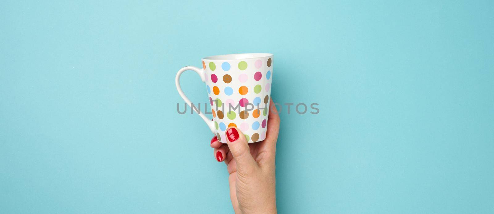 female hand holds a ceramic mug on a blue background, break time and drink coffee by ndanko