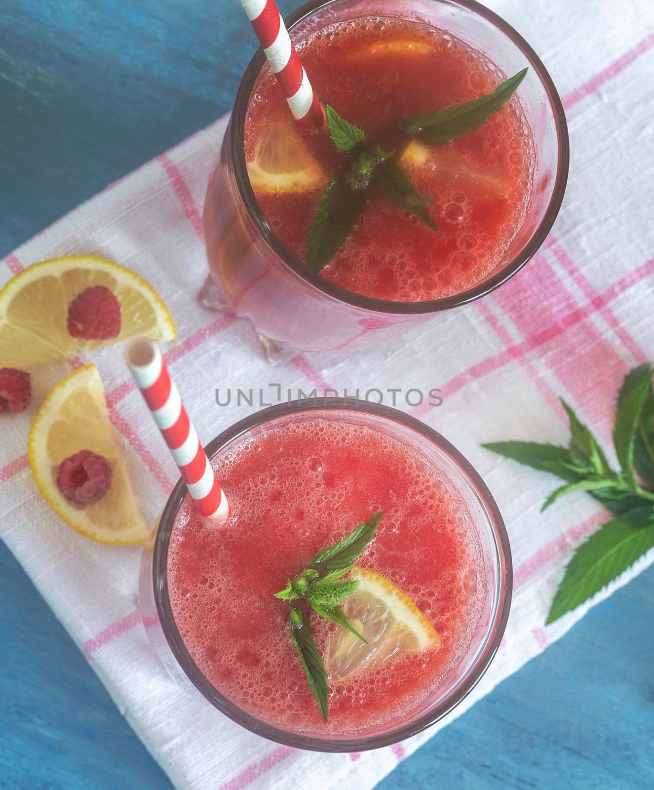 Fresh watermelon juice with raspberries and lemon in a glass. Slices of lemon and raspberry on the table. Top view. The concept of natural nutrition.