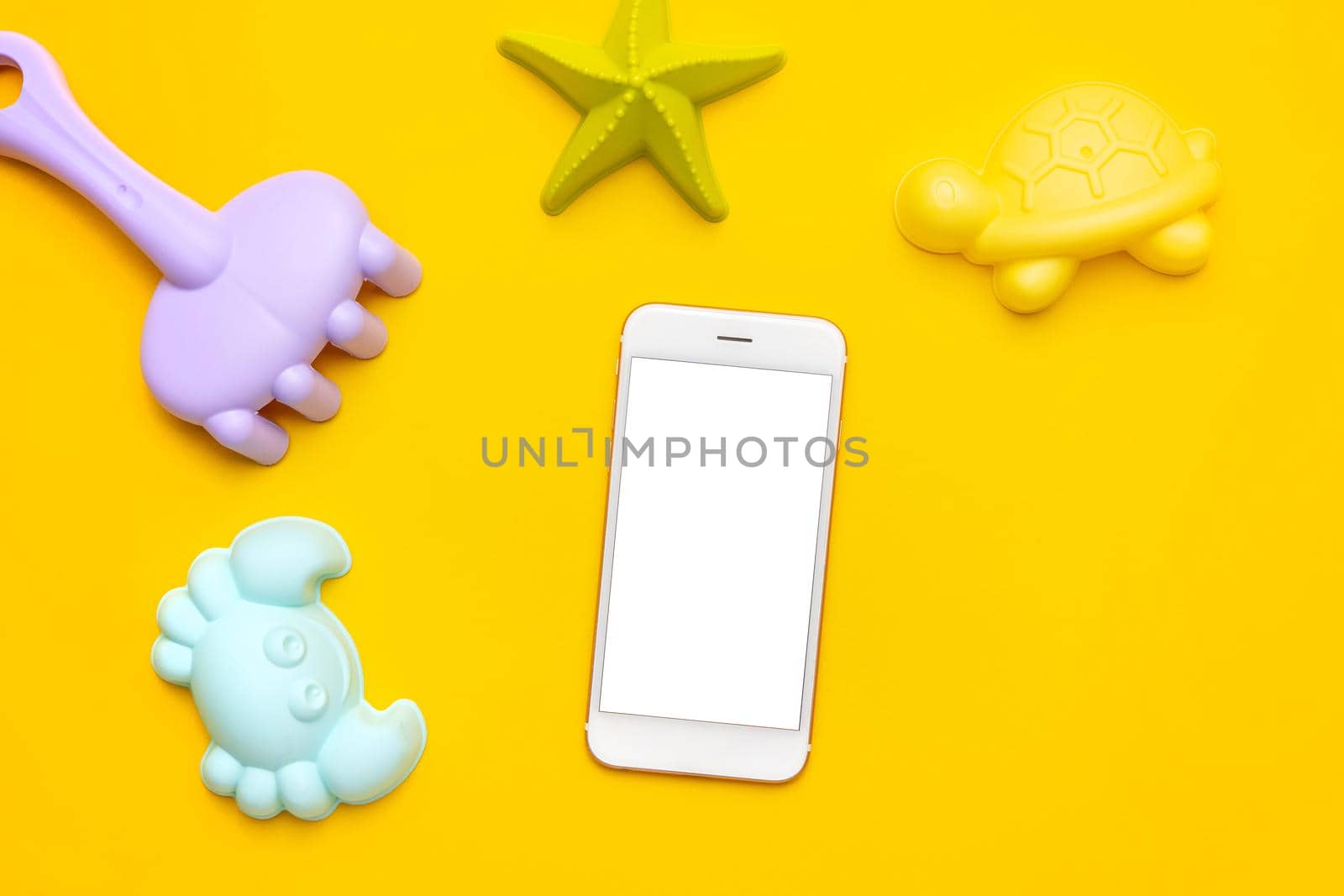 Mobile phone with white screen and plastic beach toy pastel color on yellow background. The development of fine motor concept. Creativity Game, technology and summer concept. by katrinaera