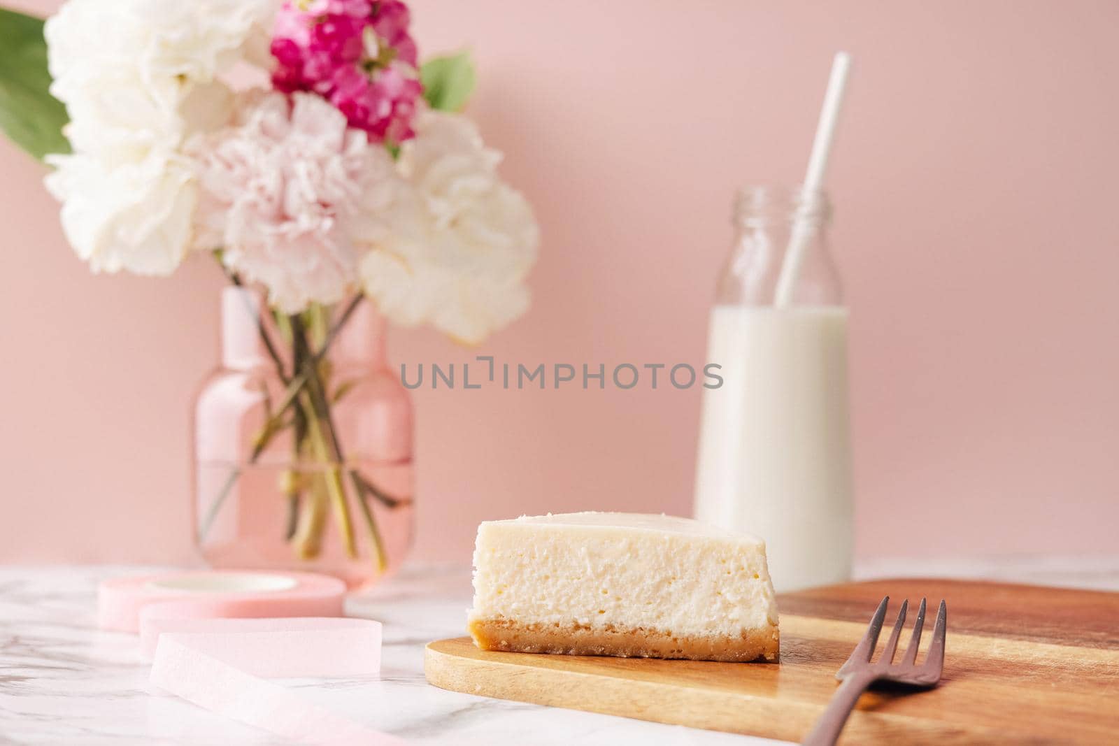 Homemade cheesecake and milk . French dessert and flowers on marble table on pink background side view