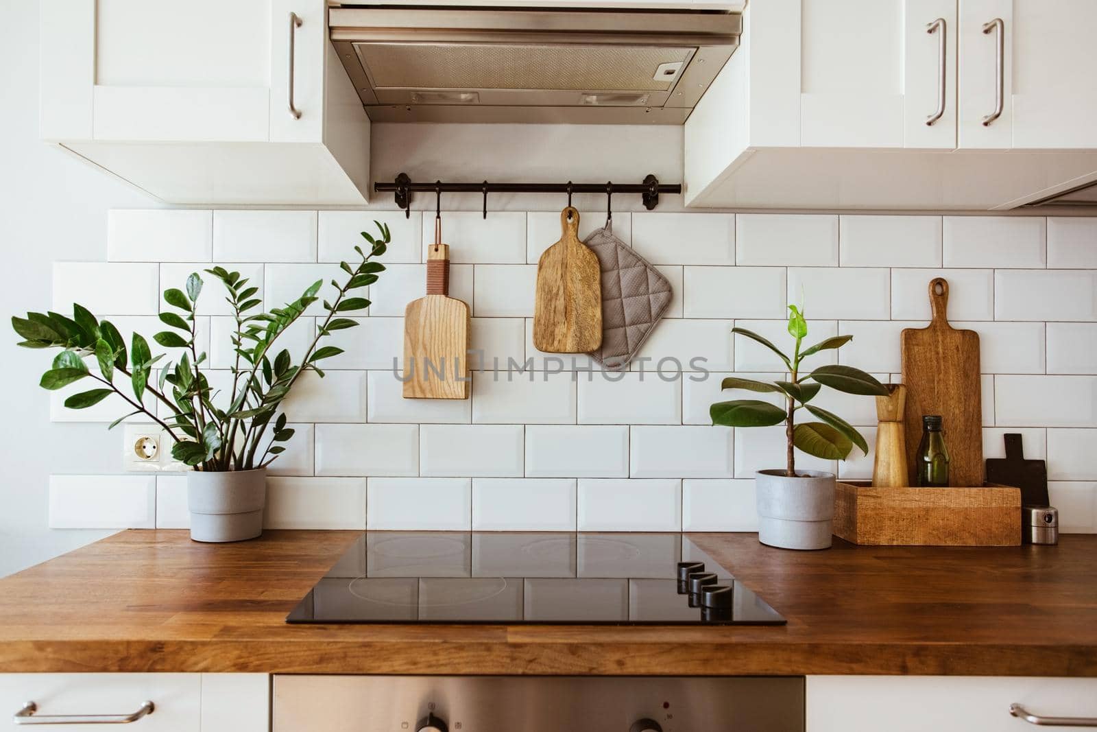 Kitchen brass utensils, chef accessories. Hanging kitchen with white tiles wall and wood tabletop.Green plant on kitchen background by katrinaera
