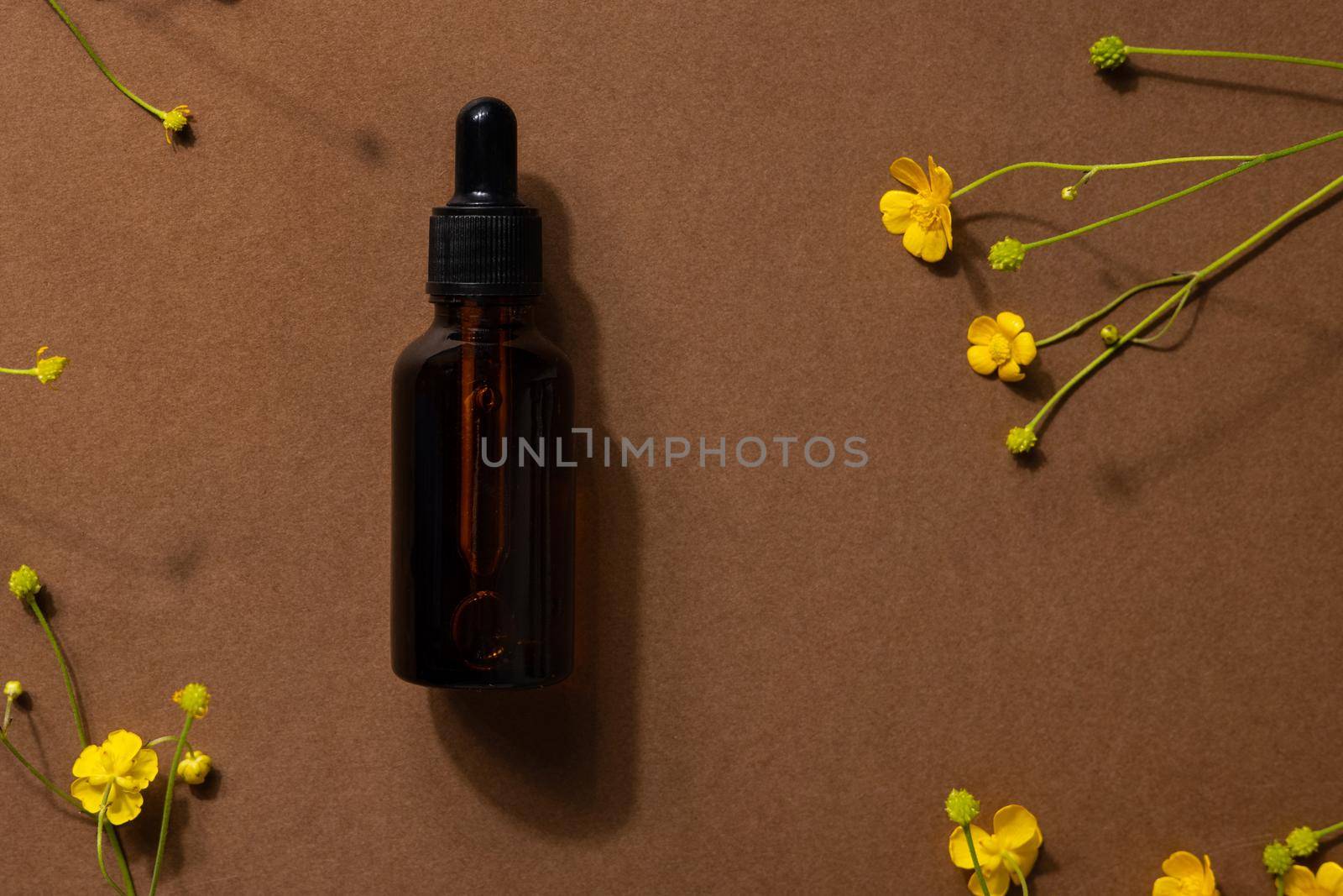 Brown glass bottle of cosmetic product or oil on stone and yellow wildflower on beige brown paper background. Natura Spa Cosmetic Beauty concept with hard shadows side view