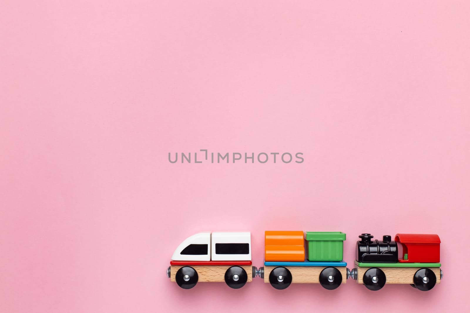 Train children toy, preschool kids game. Locomotive and carriages, wooden colorful blocks construction on pink color background side view