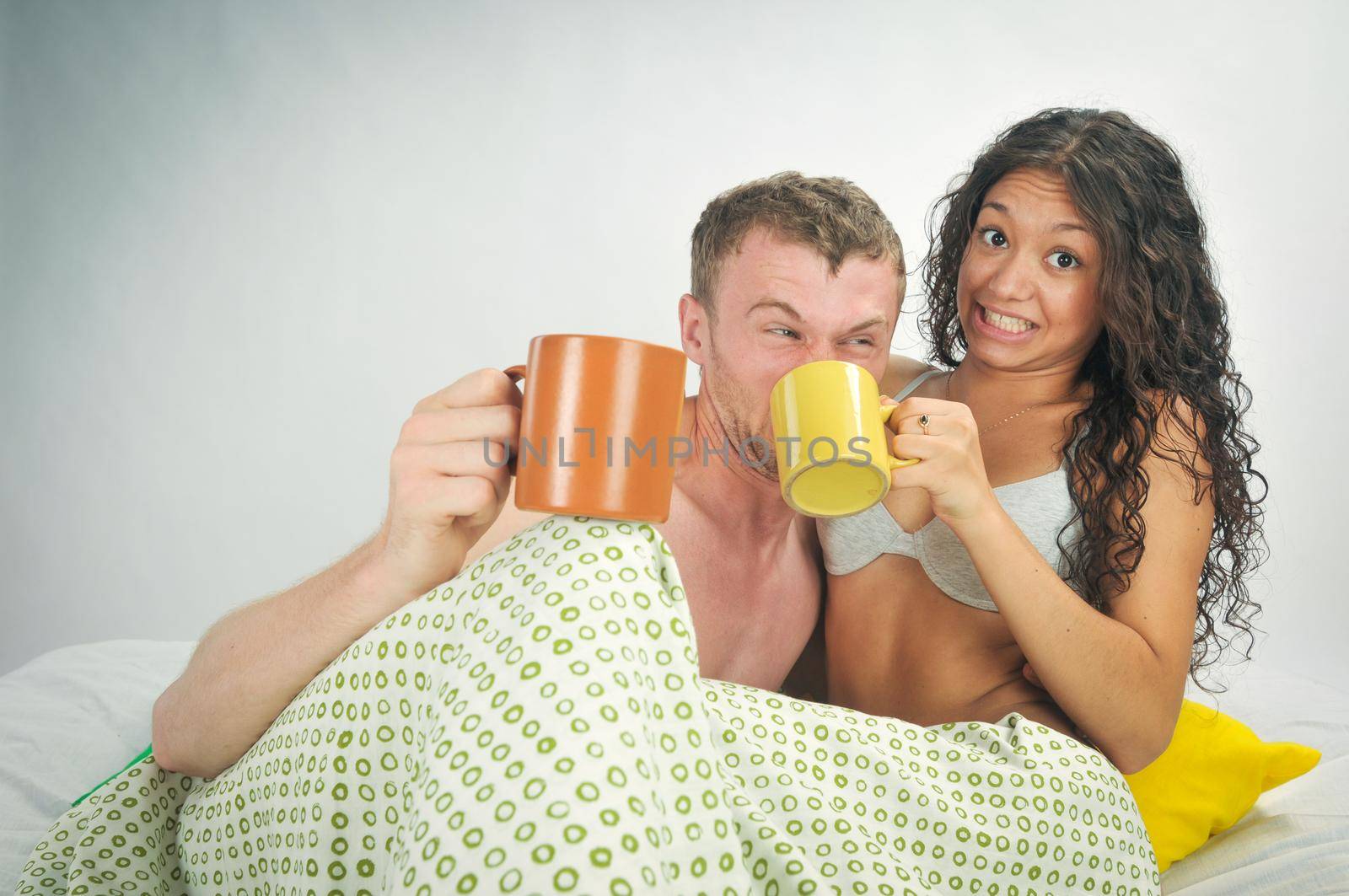 Young caucasian heterosexual couple in bed holding coffee mugs