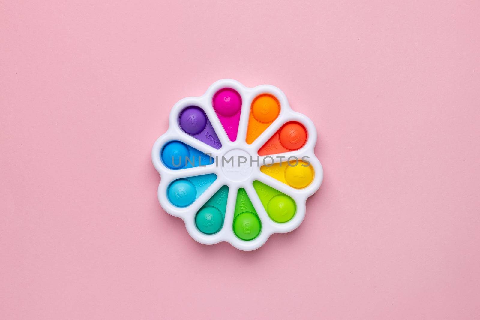 Presses with a finger anti-stress toy pop it on pink background. Colorful silicone poppit toy, bubble fidget, simple-dimple side view