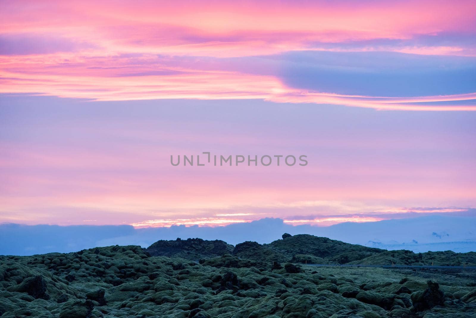 Icelandic landscape photo at sunset with volcanic rock field covered in green moss with a pretty purple and pink sky