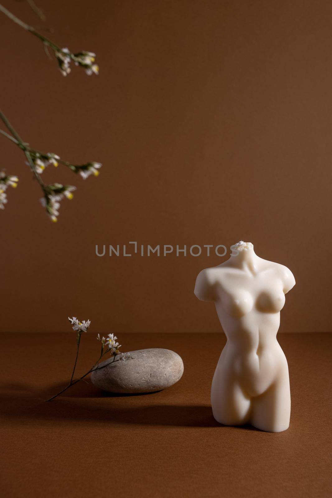 Candle in woman torso shape in brown interior with stone and dried flowers, autumn atmosphere vertical