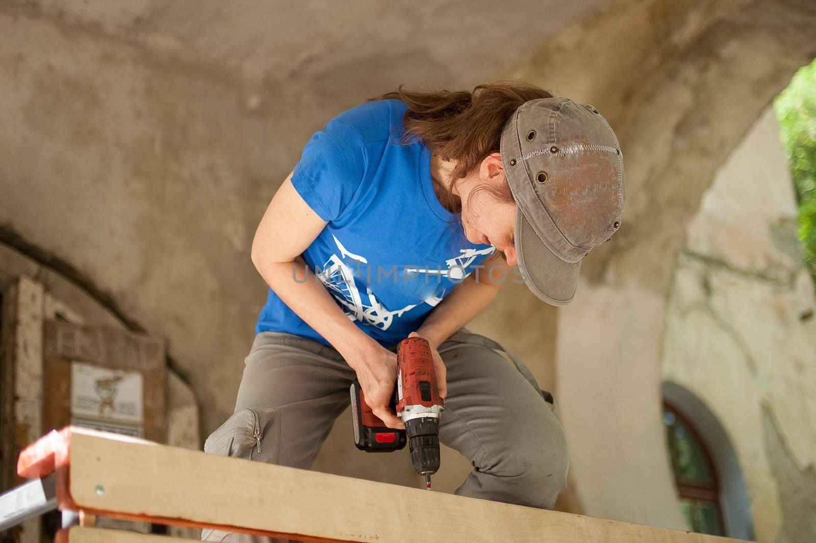 Skilled young female worker is using power screwdriver drilling during construction wooden bench gender equality, feminism, do it yourself concepts. by balinska_lv