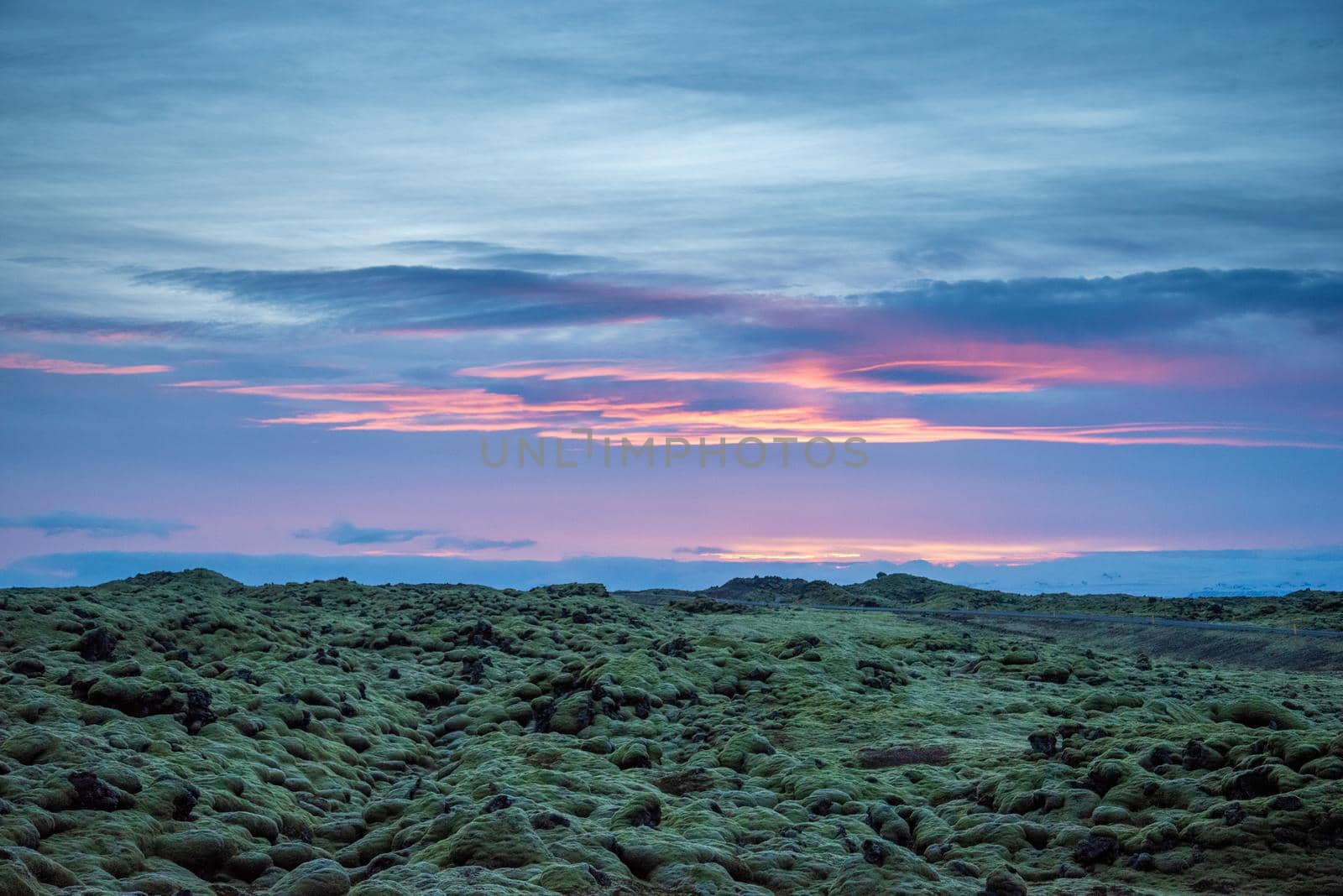 Icelandic landscape photo at sunset with volcanic rock field covered in green moss with a pretty purple and pink sky