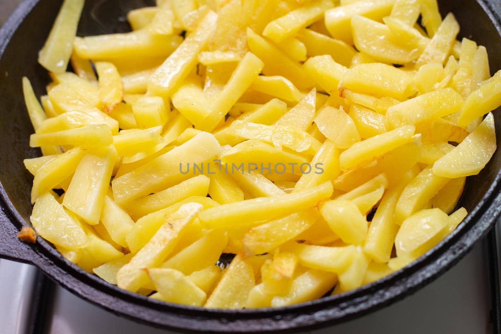 Potatoes cut into strips are fried in a pan. Delicious vegetable dish.