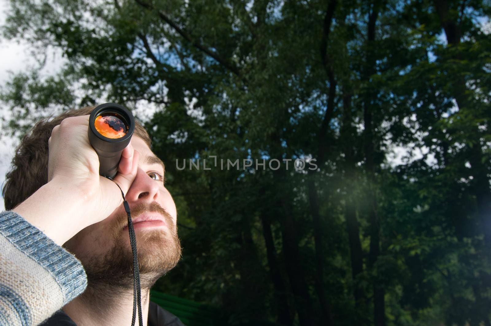 Young man hangs out in a park looking up with his spyglass.