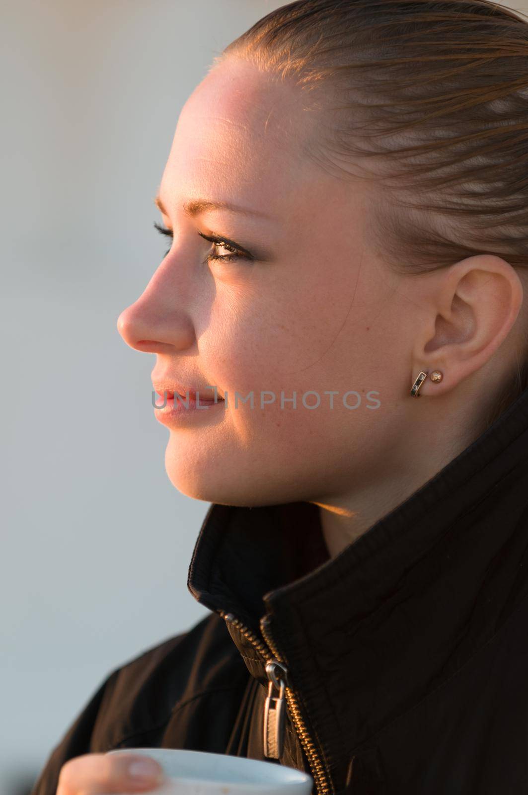 Young woman watching sunrise holding cup of coffee