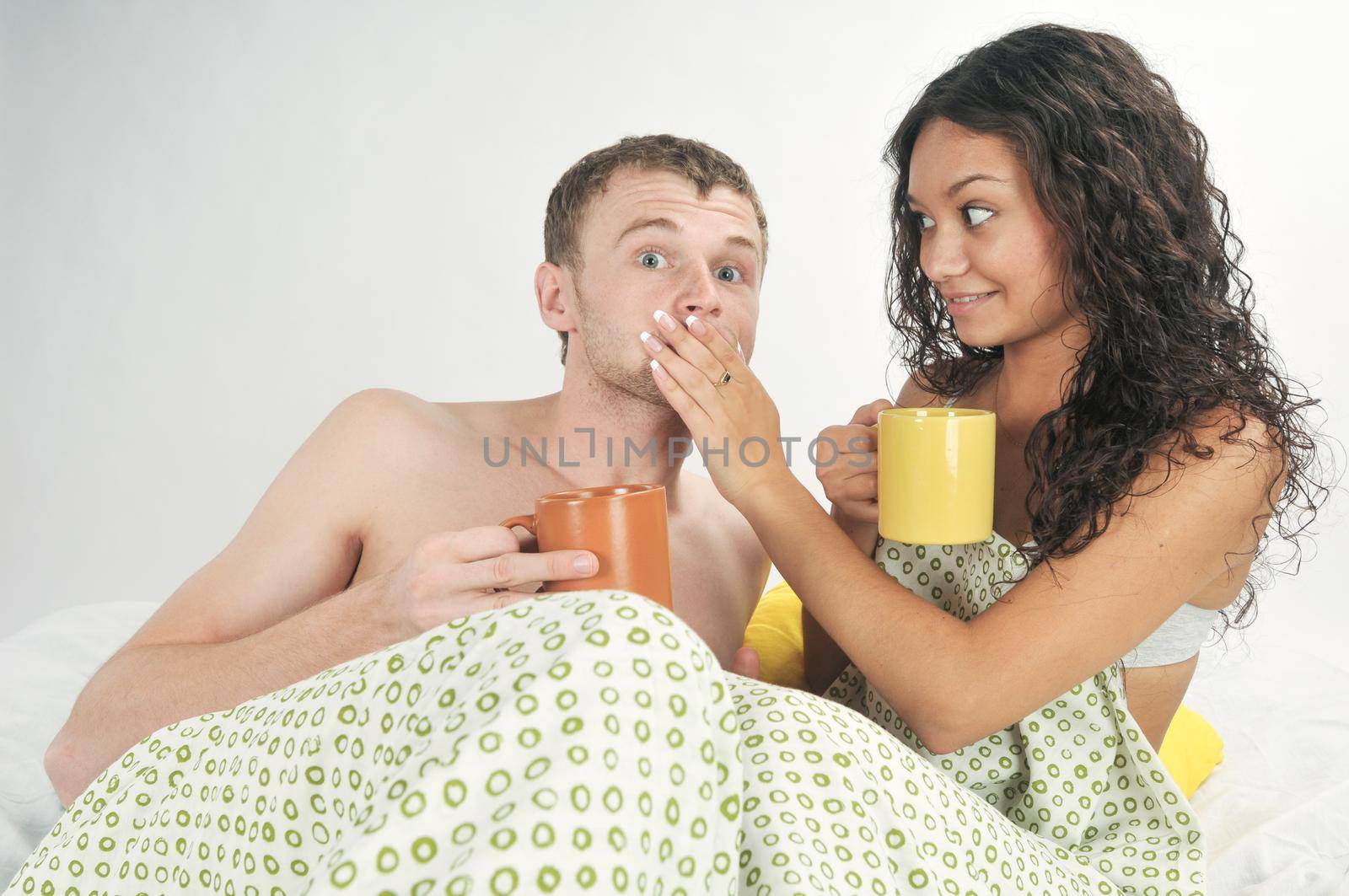 Young caucasian heterosexual couple in bed holding coffee mugs