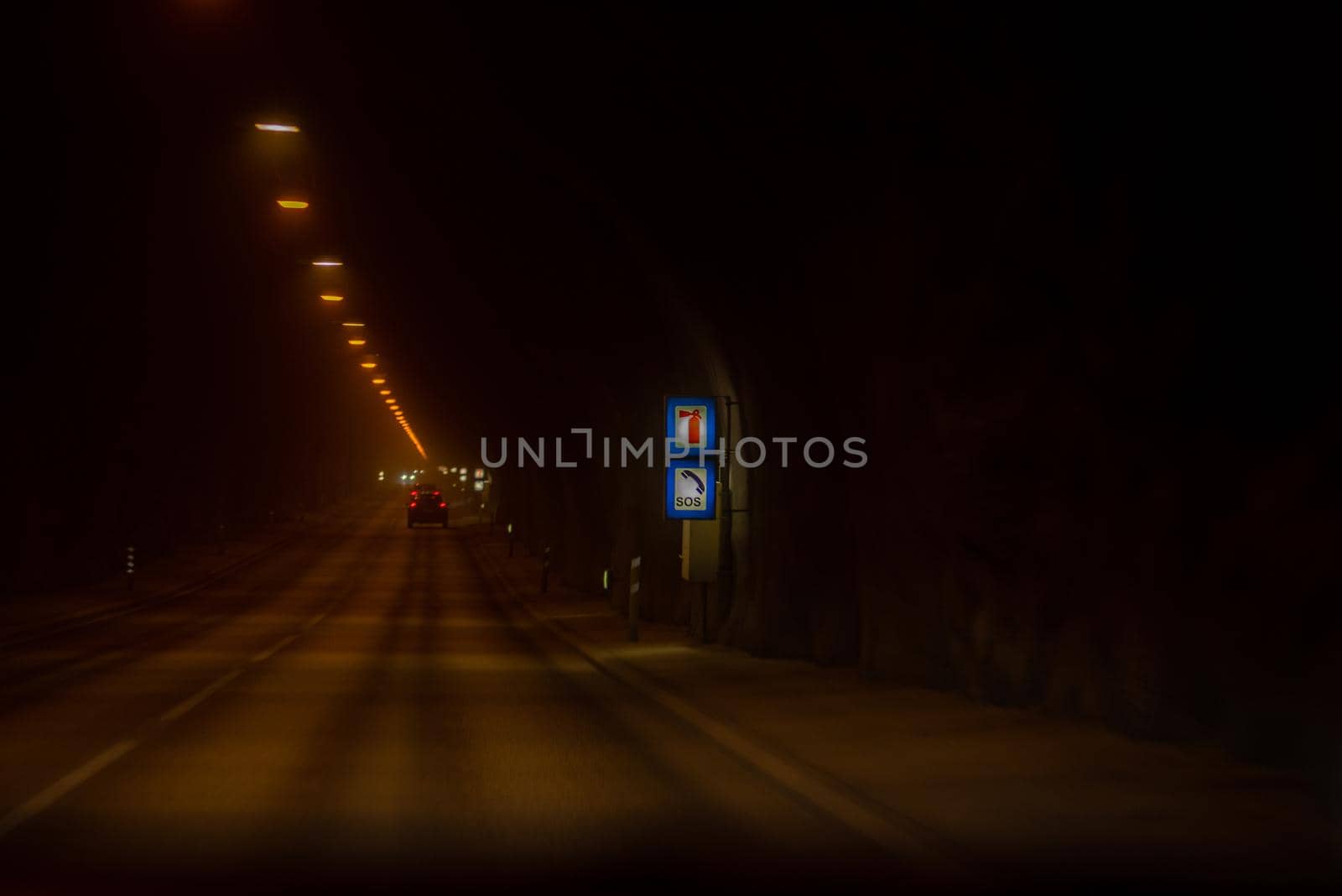 Dark underground tunnel long paved road with dim warm lighting and SOS signage