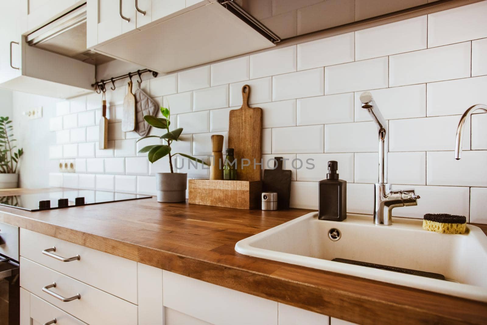 Kitchen brass utensils, chef accessories. Hanging kitchen with white tiles wall and wood tabletop.Green plant on kitchen background by katrinaera