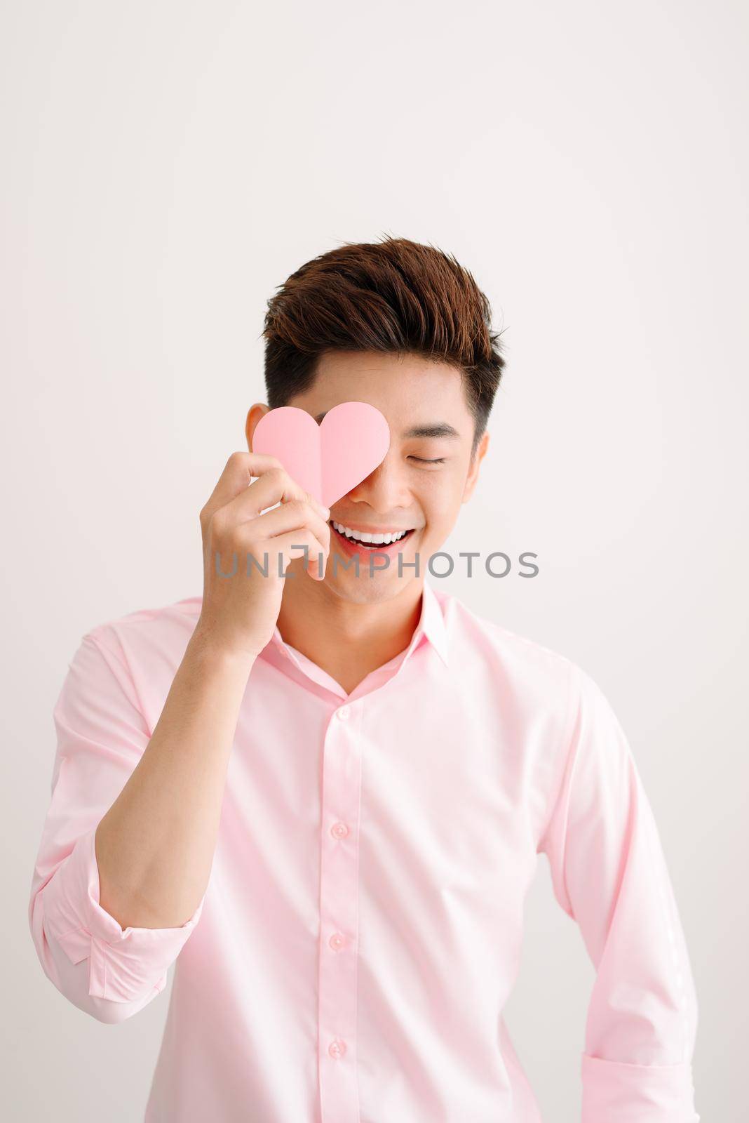 Handsome asian man holding pink heart paper posing on gray background