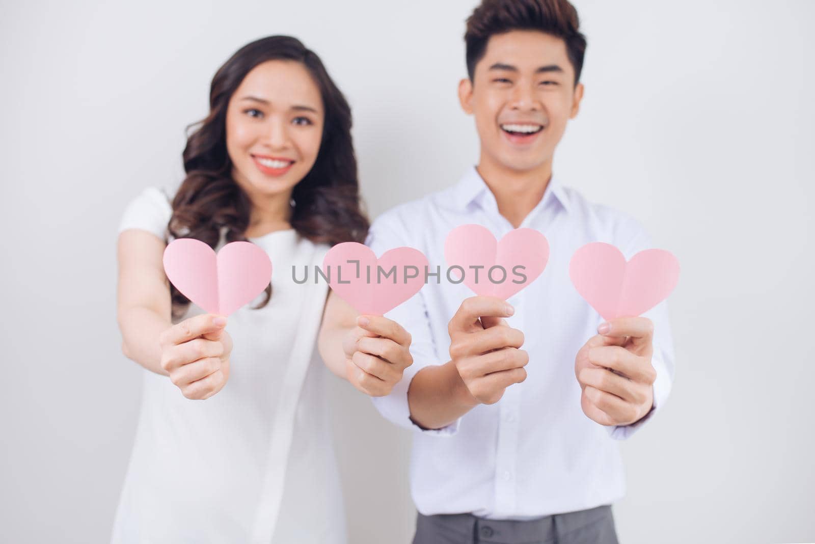 Happy young Vietnamese couple is holding pink paper hearts and smiling