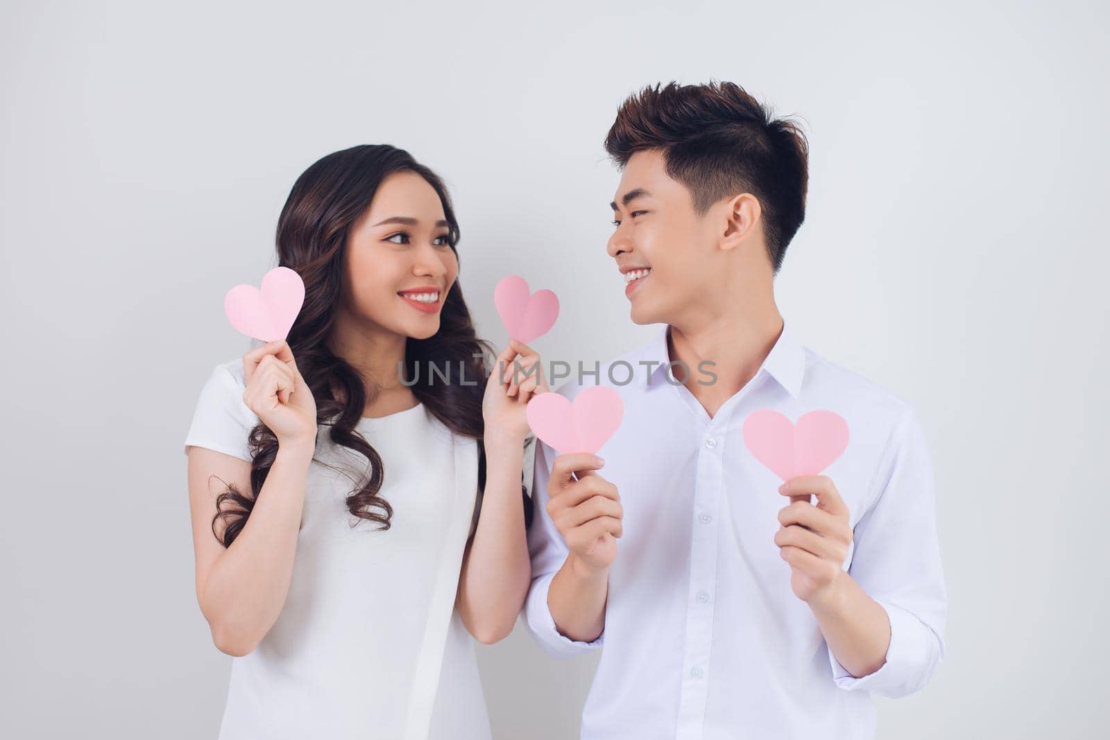 Happy young Vietnamese couple is holding pink paper hearts and smiling