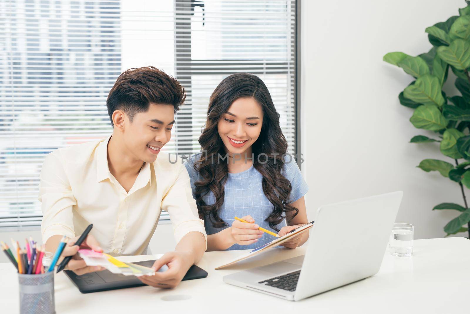 Two smiling casual designers working with laptop while sitting at desk in the office