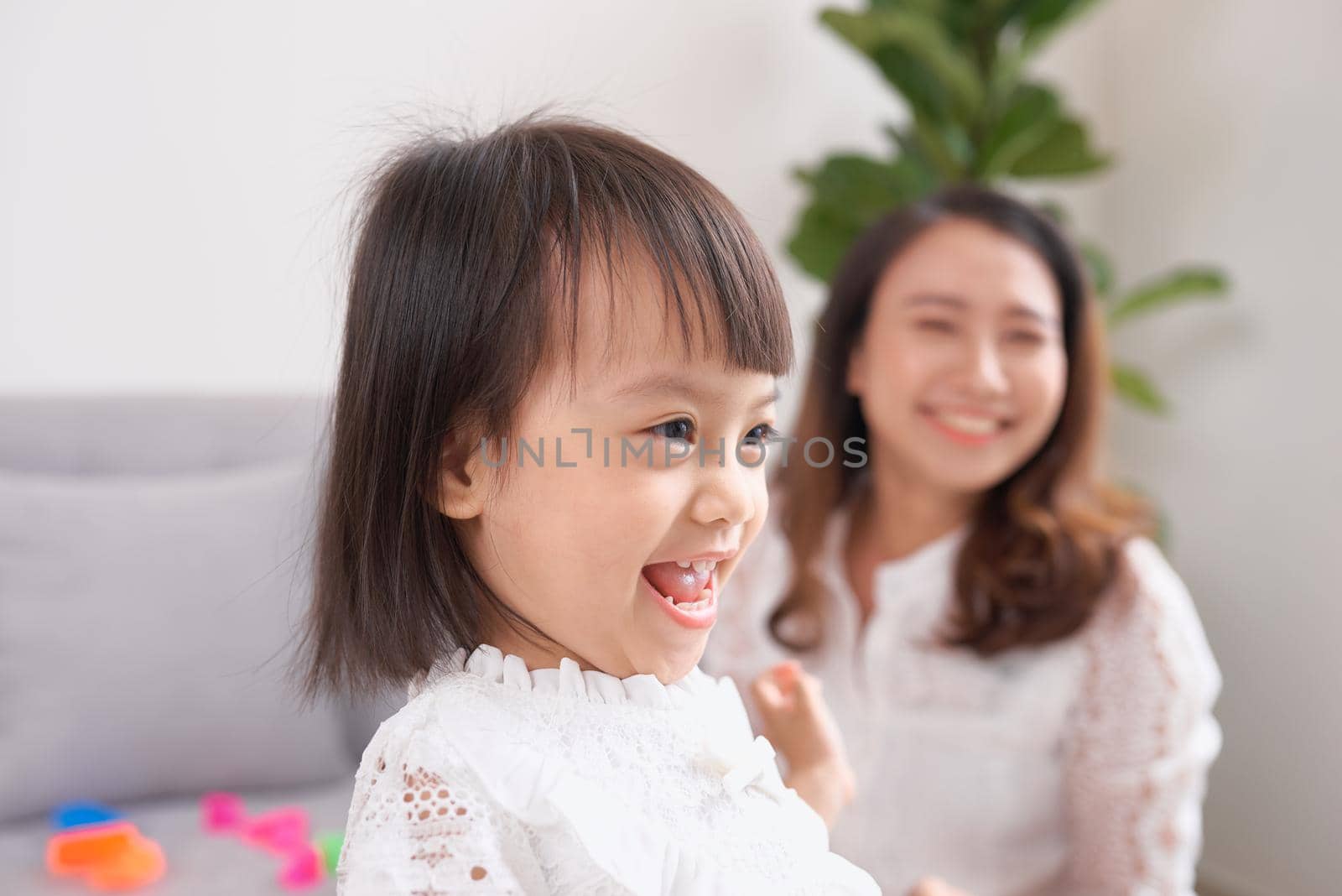 Little girl and her mom drinking milk sitting on sofa at home. Motherhood and care, healthy eating and lifestyle, early development concept, copy space