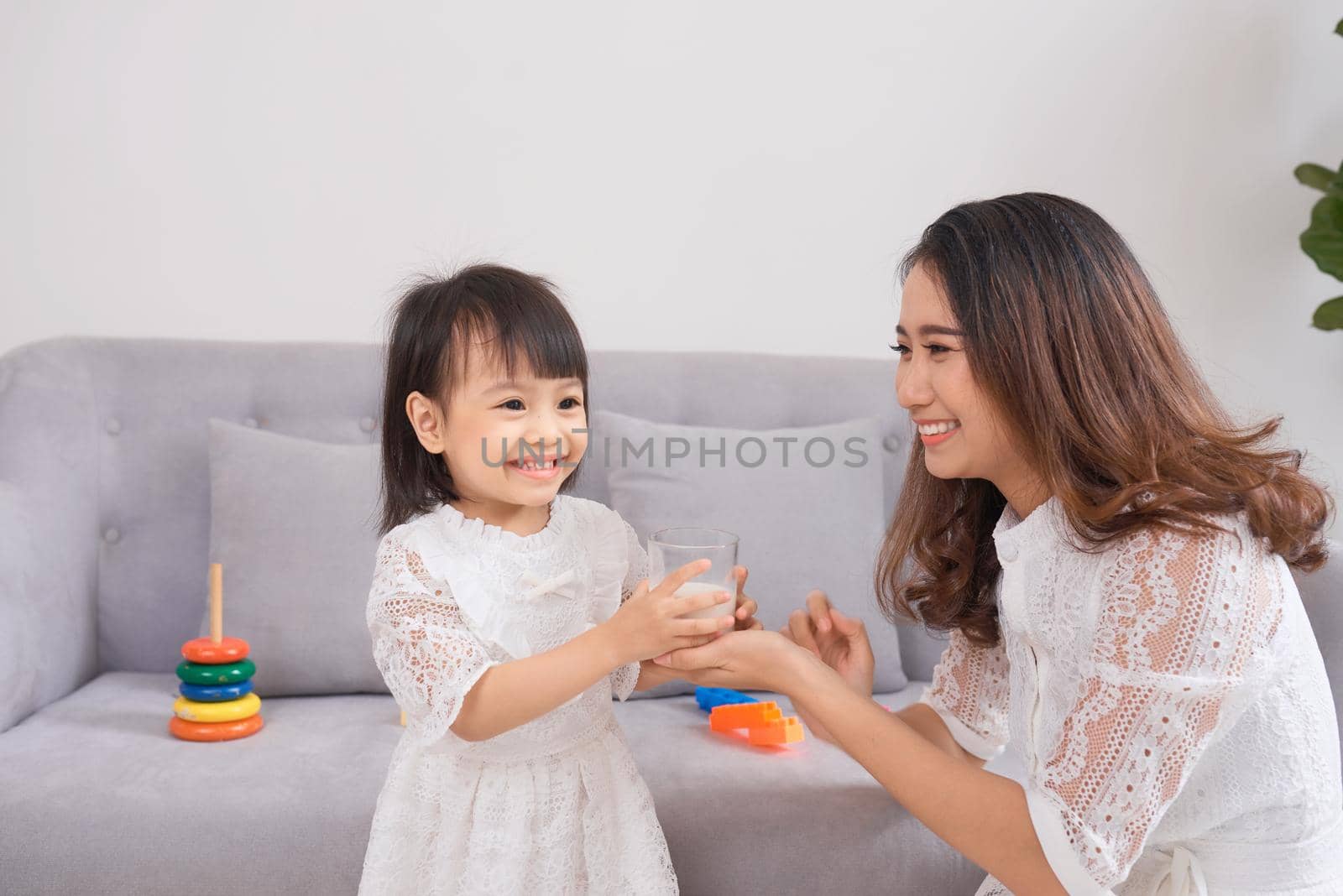 Little girl and her mom drinking milk sitting on sofa at home. Motherhood and care, healthy eating and lifestyle, early development concept, copy space by makidotvn