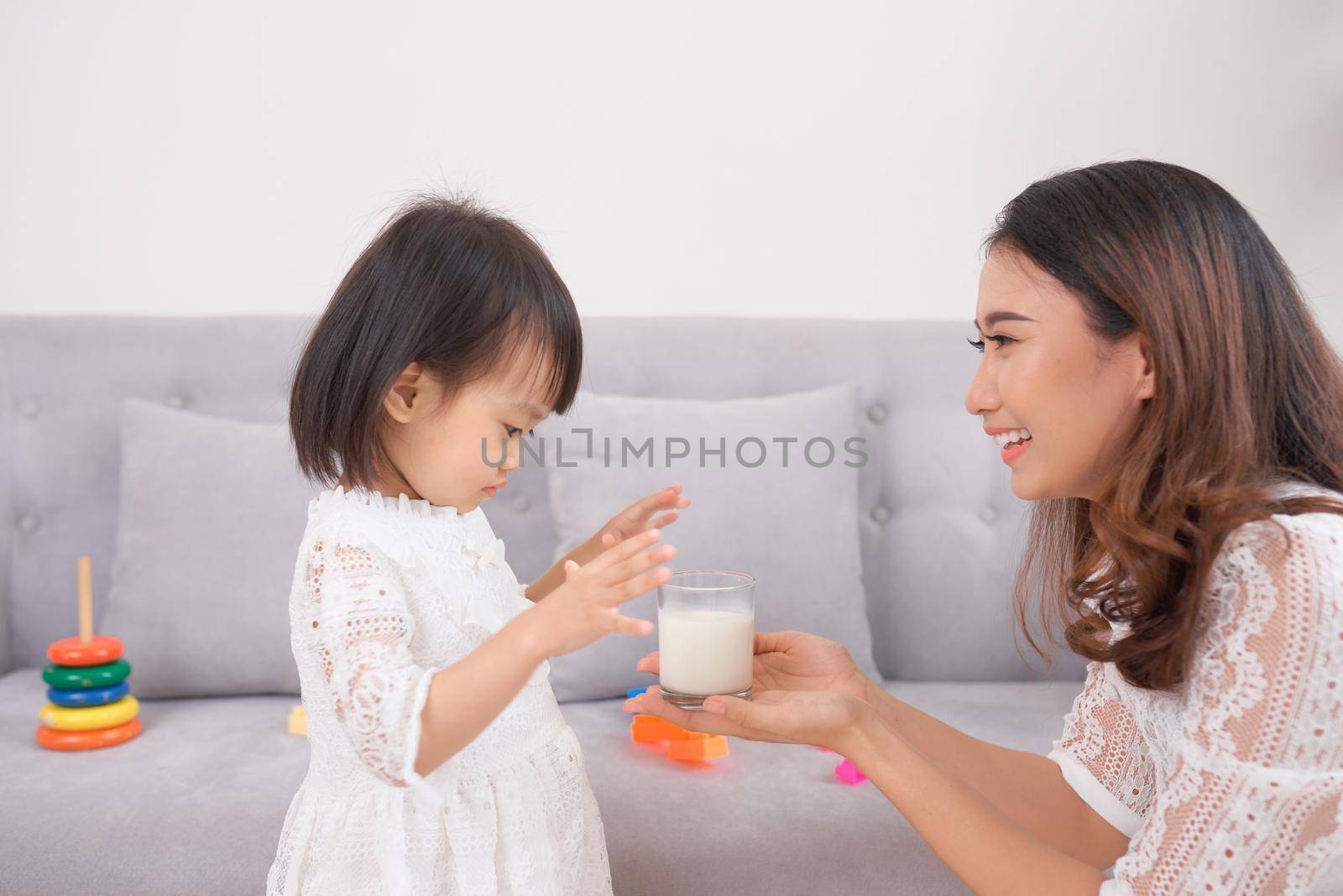 Little girl and her mom drinking milk sitting on sofa at home. Motherhood and care, healthy eating and lifestyle, early development concept, copy space