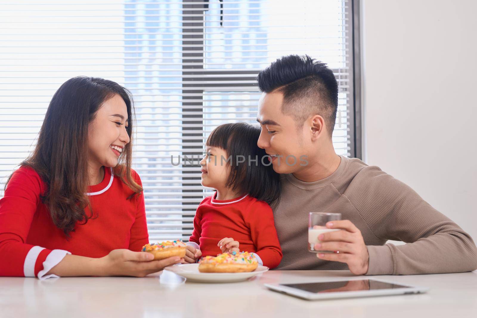 Happy young family with children enjoying breakfast in a white sunny dining room with a big garden view window by makidotvn