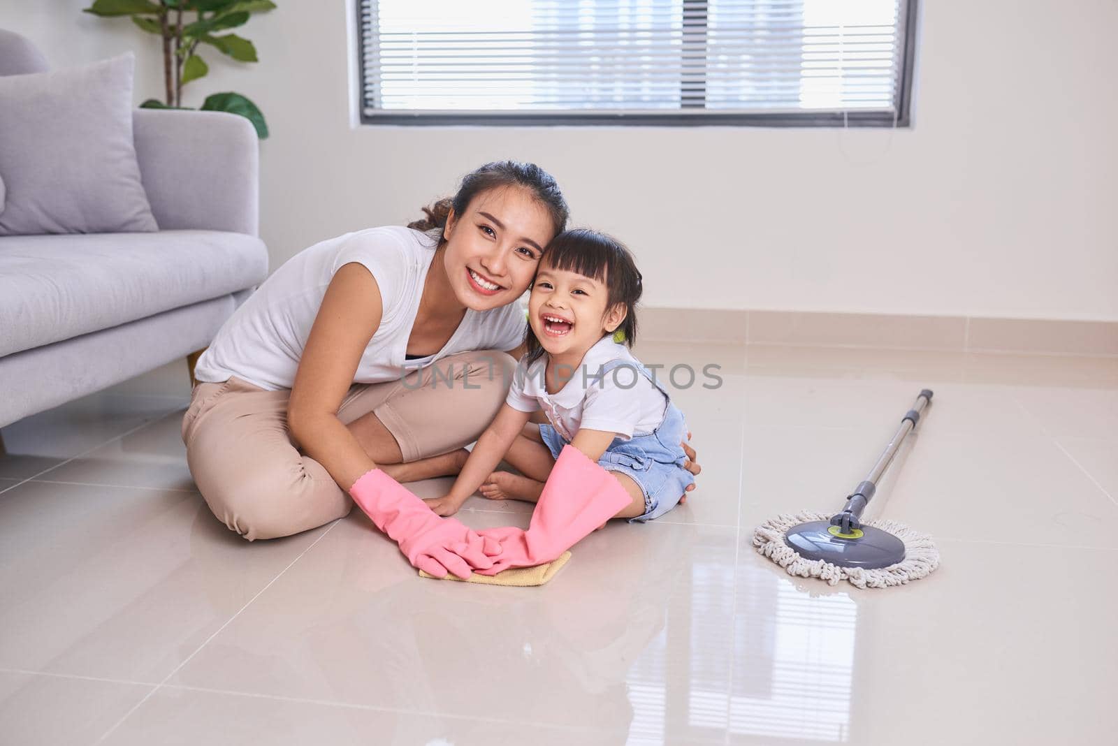 mum teaching daughter cleaning their home living room at weekend. A young woman and a little child girl dusting. family housework and household concept. by makidotvn