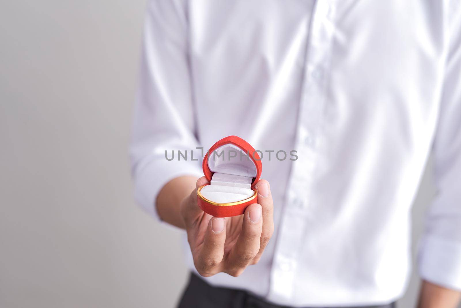 Handsome elegant man in a white shirt is holding a box with an engagement ring and shows in camera. by makidotvn