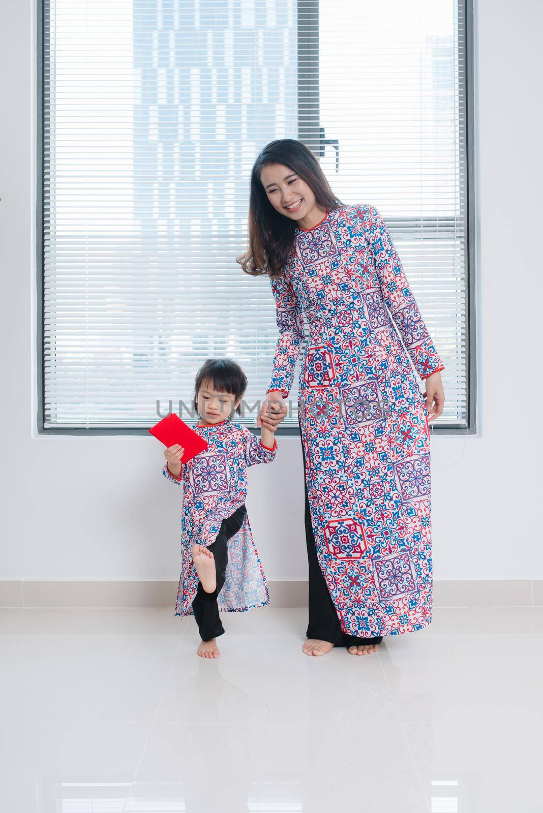 Vietnamese mother and daughter in Ao Dai Traditional dress, celebrate new year at home. Tet Holiday.