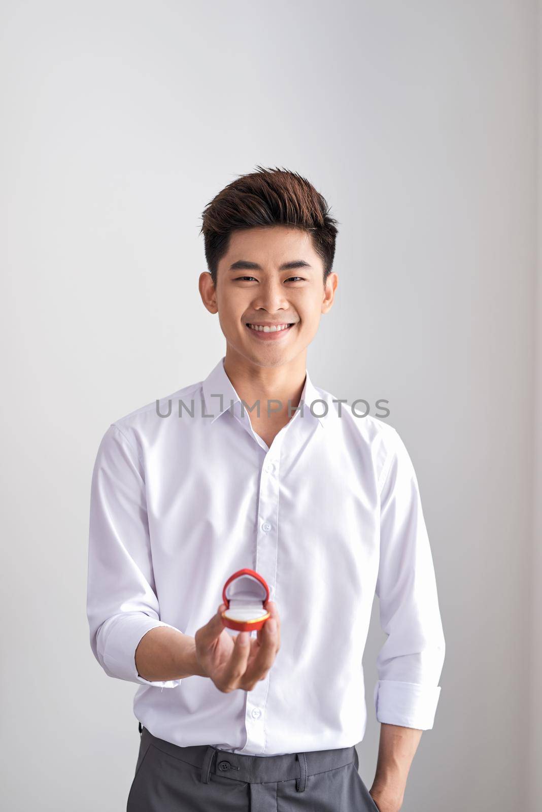 Handsome elegant man in a white shirt is holding a box with an engagement ring and shows in camera.