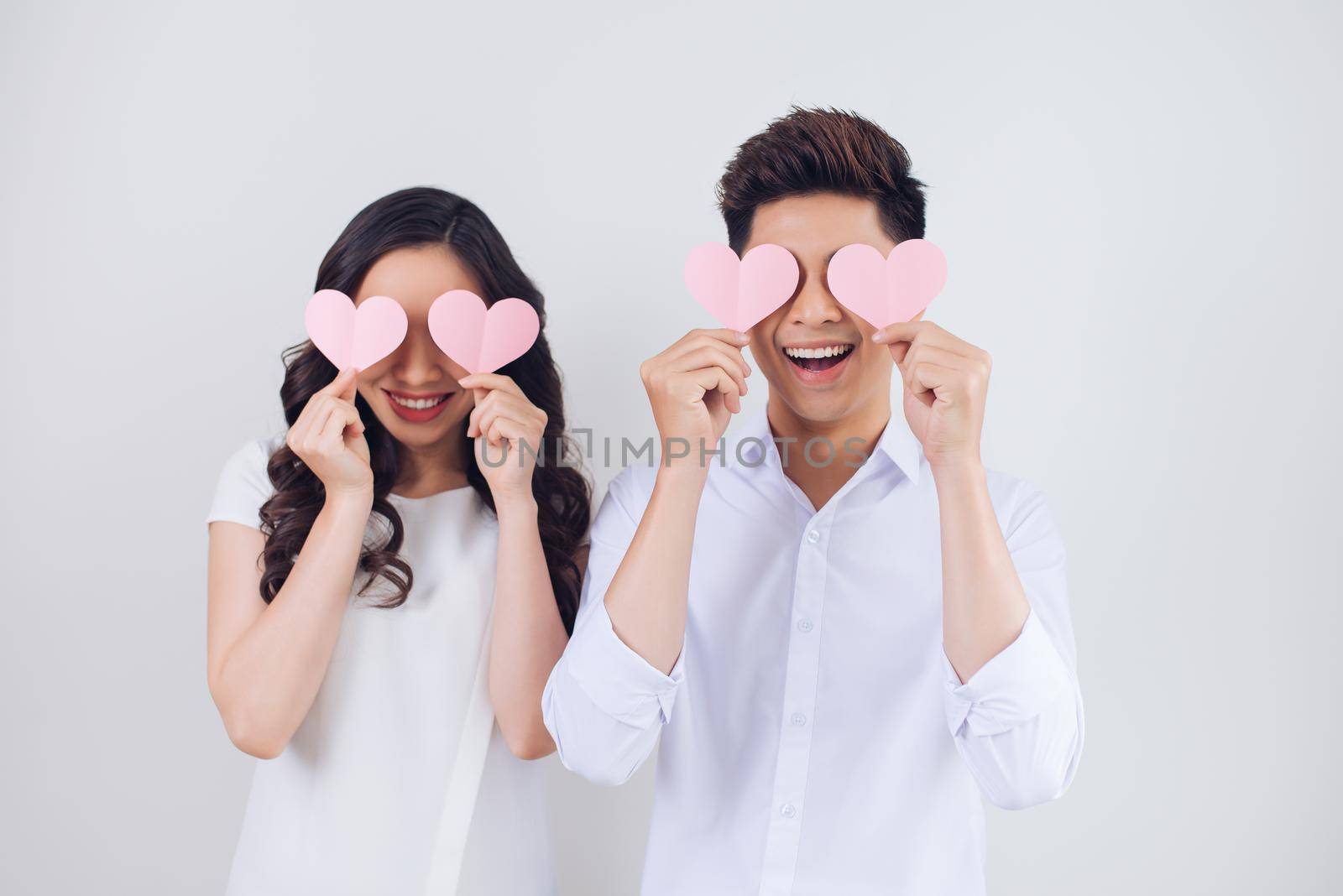 Happy young Vietnamese couple is holding pink paper hearts and smiling