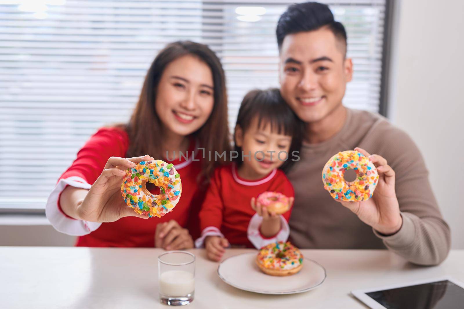 Happy young family with children enjoying breakfast in a white sunny dining room with a big garden view window