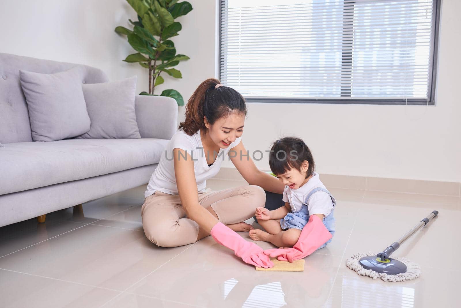 mum teaching daughter cleaning their home living room at weekend. A young woman and a little child girl dusting. family housework and household concept. by makidotvn